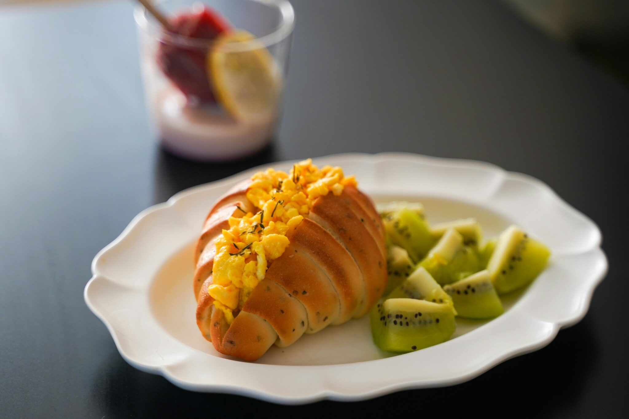 A close-up of a breakfast with egg-filled bread, kiwi slices, and a glass of smoothie.
